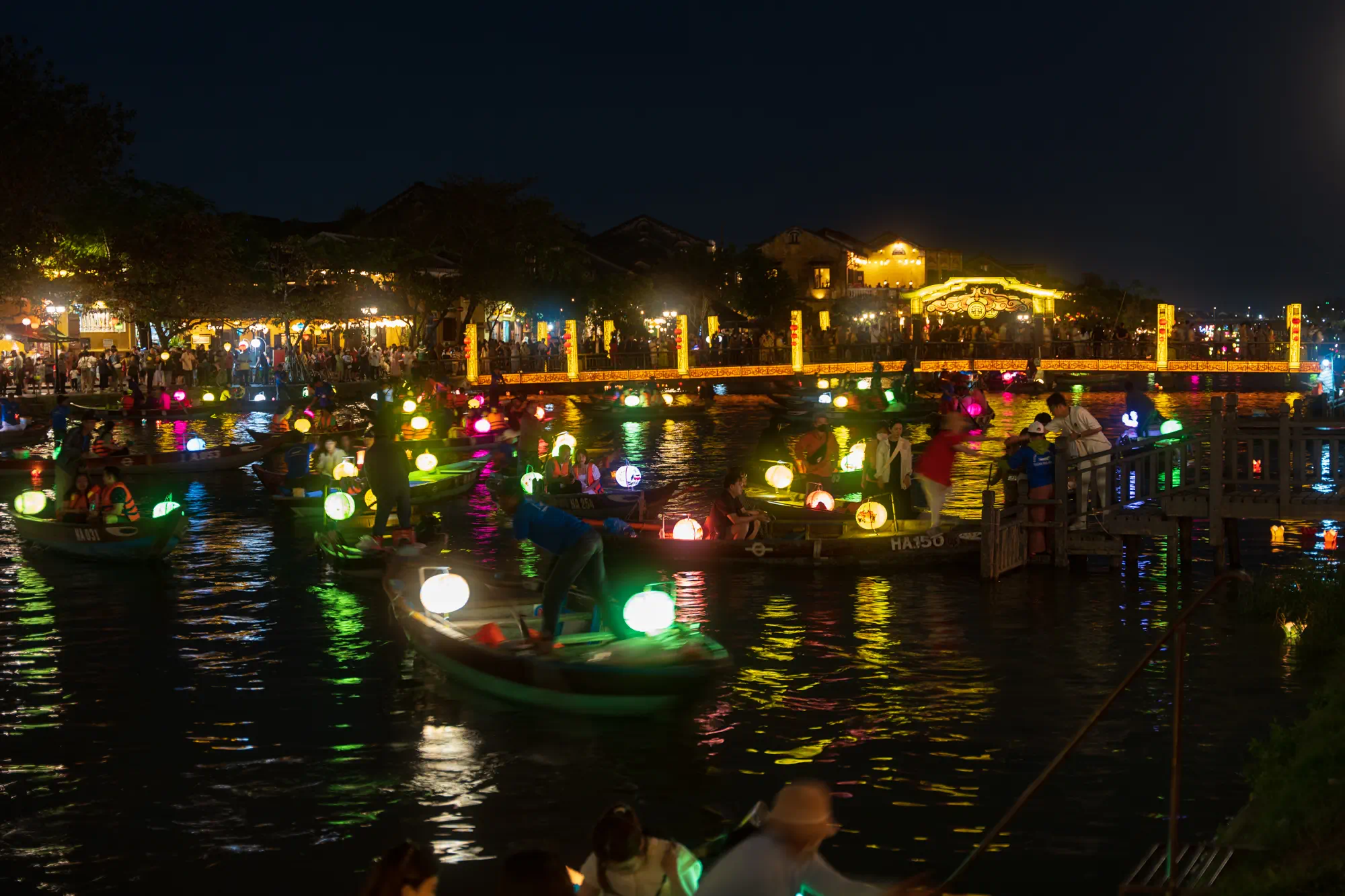 夜の川にうかぶ多数の手こぎボート。それぞれの上には提灯が光っている。